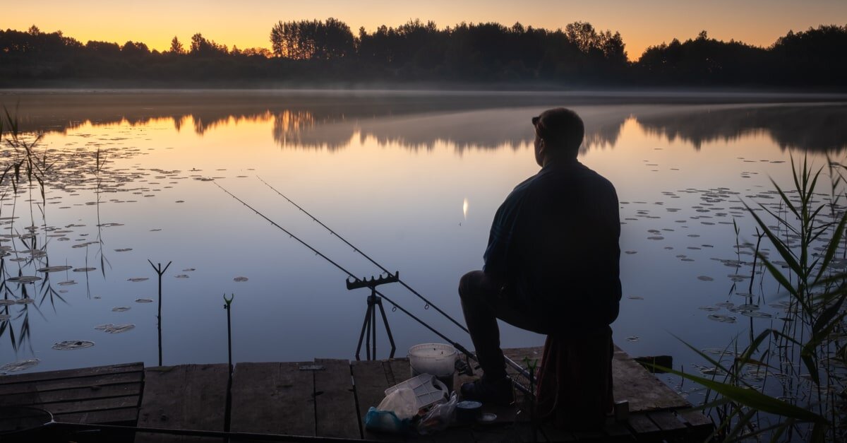 Nachts sitzt ein Fischer an einer Angelstelle mit Angelruten am See