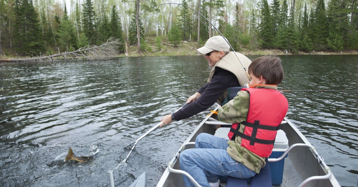 Junge und Mann sitzend im Angelboot auf einem See, während der Junge einen Fisch an der Angel hat.