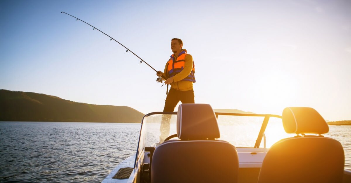 Aufnahme von einem Angler, der auf einem Angelboot steht und angelt. Im Hintergrund ein See.