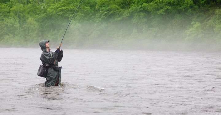 Angler der bei Regen mit einer Wathosen in einem Gewässer angelt