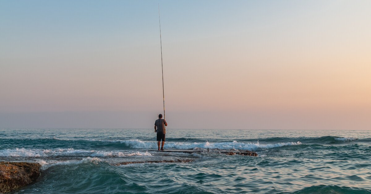 Aufnahme eines Anglers am Strand. Im Hintergrund Meer.