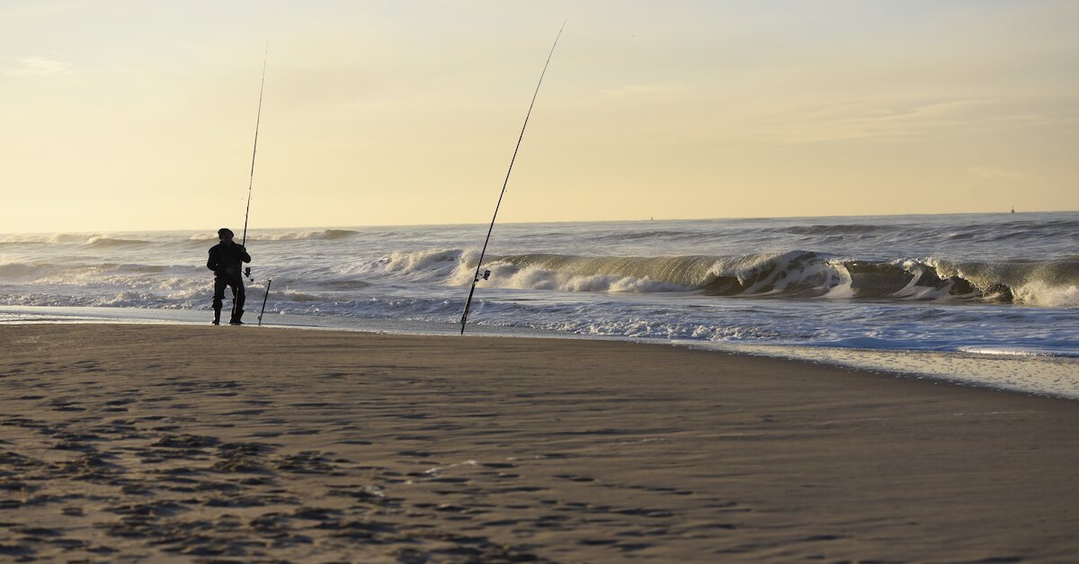 Aufnahme eines Anglers an einem Strand in Holland. Im Hintergrund die Wellen des Meeres.