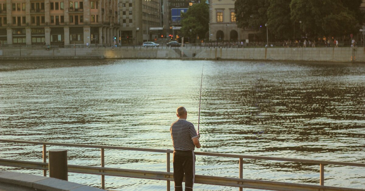 Aufnahme eines Anglers, der in der Stadt angelt. Im Hintergrund Stadtbild.