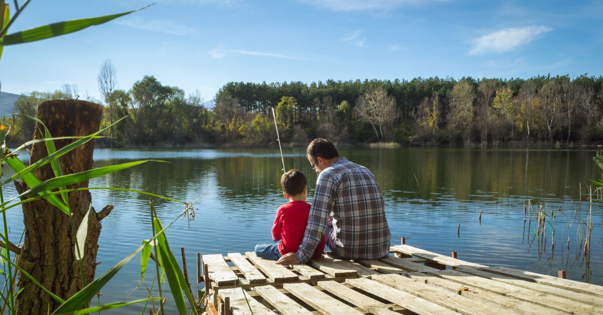 Aufnahme von Vater und Sohn, sitzend am Gewässer mit Angel in der Hand.