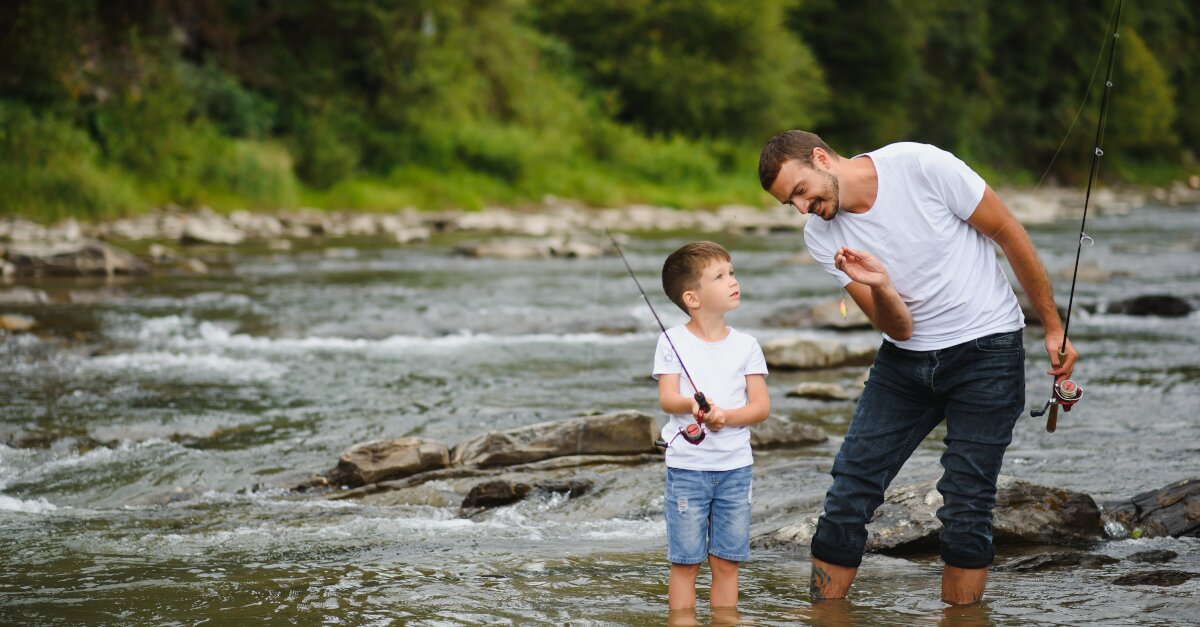 Vater und Sohn stehen mit einer Angelrute in einem Fluss.