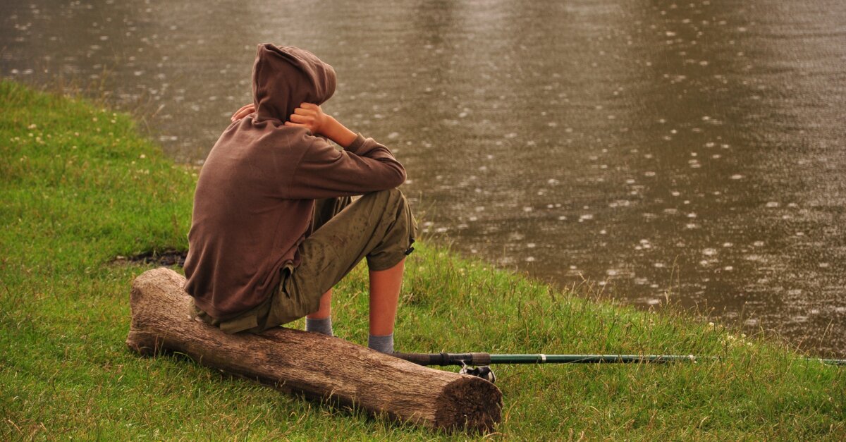 Aufnahme von einem Angler, der an einem Teich sitzt und angelt bei Regen.