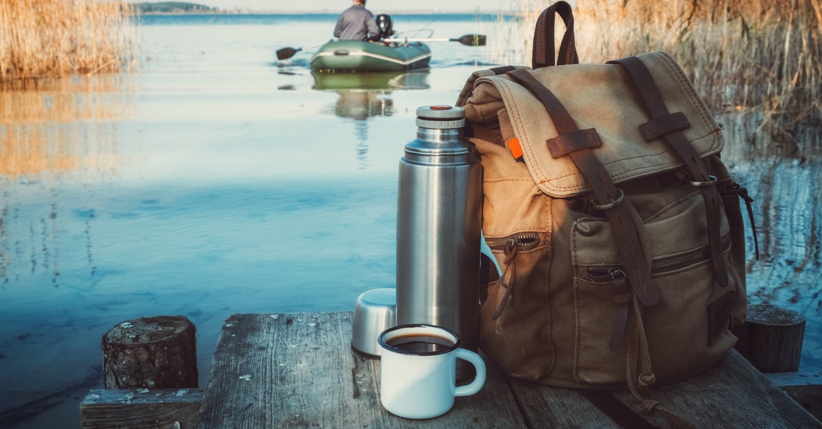 Im Vordergrund Angelrucksack mit Kaffee. Im Hintergrund Angler auf einem Angelboot, der zum Angeln fährt“.