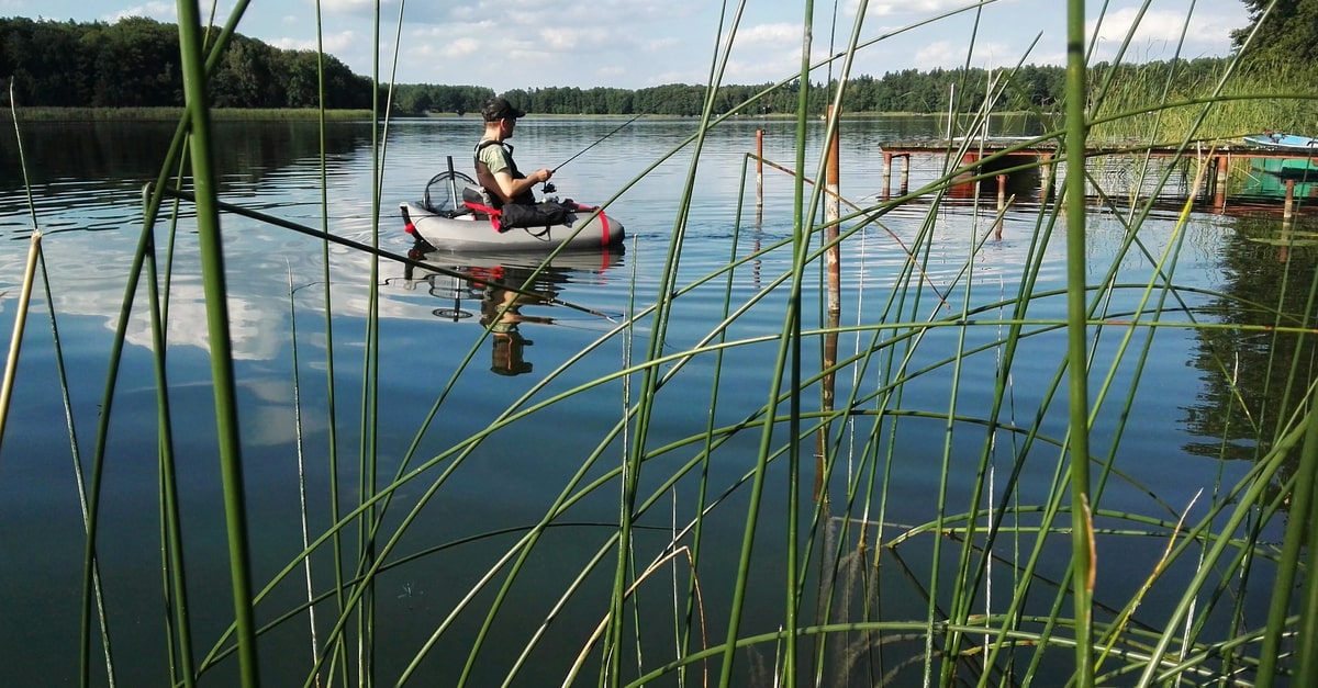 Angler sitzt im See in einem Belly Boot. Im Vordergrund Schilf